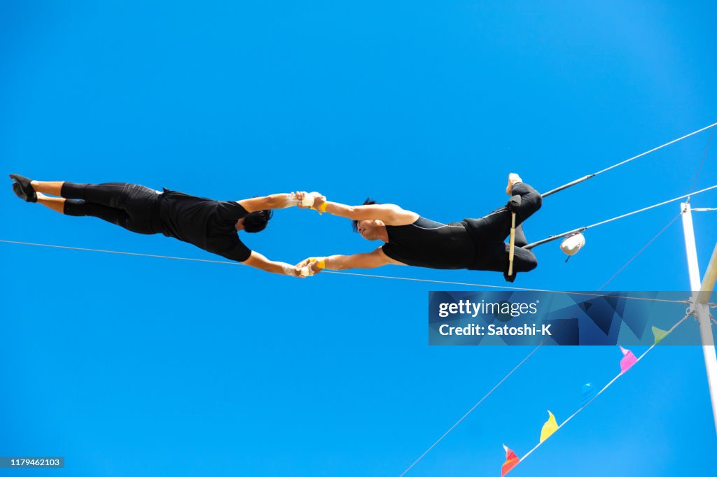 Two trapeze artists flying together in the sky