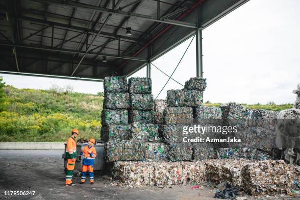 mitarbeiter sprechen neben stapeln von verdichteten wertstoffen - clothes waste stock-fotos und bilder