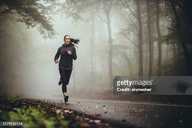 junge athletische frau joggen auf der straße in nebligen wald. - jogging stock-fotos und bilder