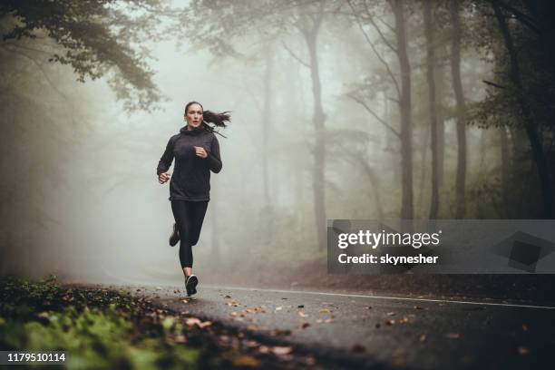 junge athletische frau joggen auf der straße in nebligen wald. - autumn forest stock-fotos und bilder