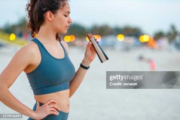 ung kvinna på en paus från jogging, äta protein bar - open workouts bildbanksfoton och bilder