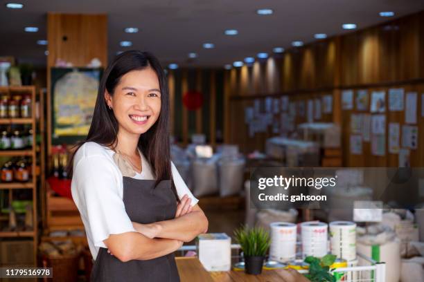 mature female grocery store owner, standing arm crossed in the shop - community arm in arm stock pictures, royalty-free photos & images