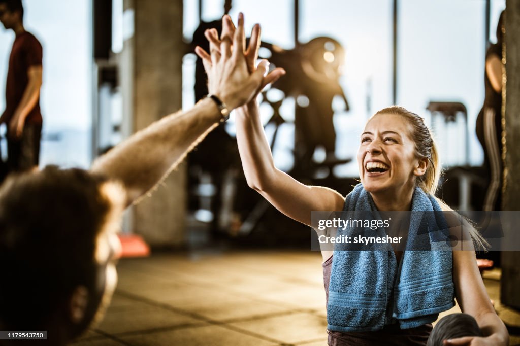 Glückliche athletische Frau gibt High-Five zu ihrem Freund auf einer Pause in einem Fitness-Studio.