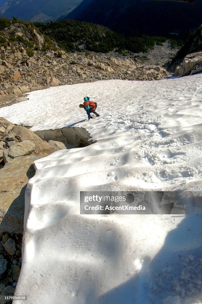 Male hiker makes his way down mountain snow patch