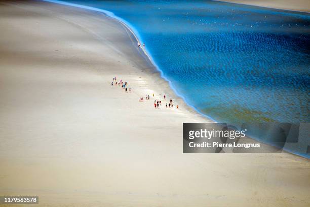 group of tourists hiking along flowing sea water in the bay of mont saint-michel - crowded beach stock pictures, royalty-free photos & images