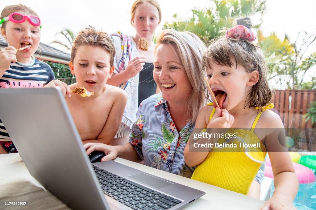 Australian family use a desktop devices together on the back deck whilst eating icecream.