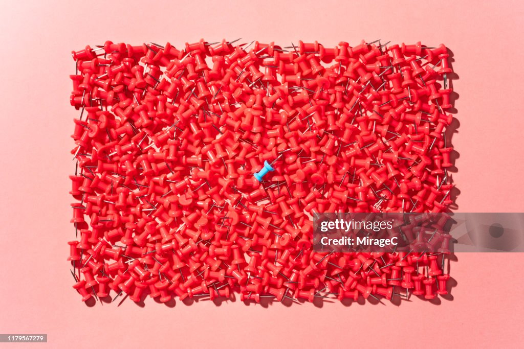 Blue Thumbtack in a Pile of Red Thumbtacks