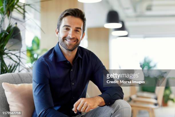 portrait of happy entrepreneur sitting in office - formal portrait stock-fotos und bilder