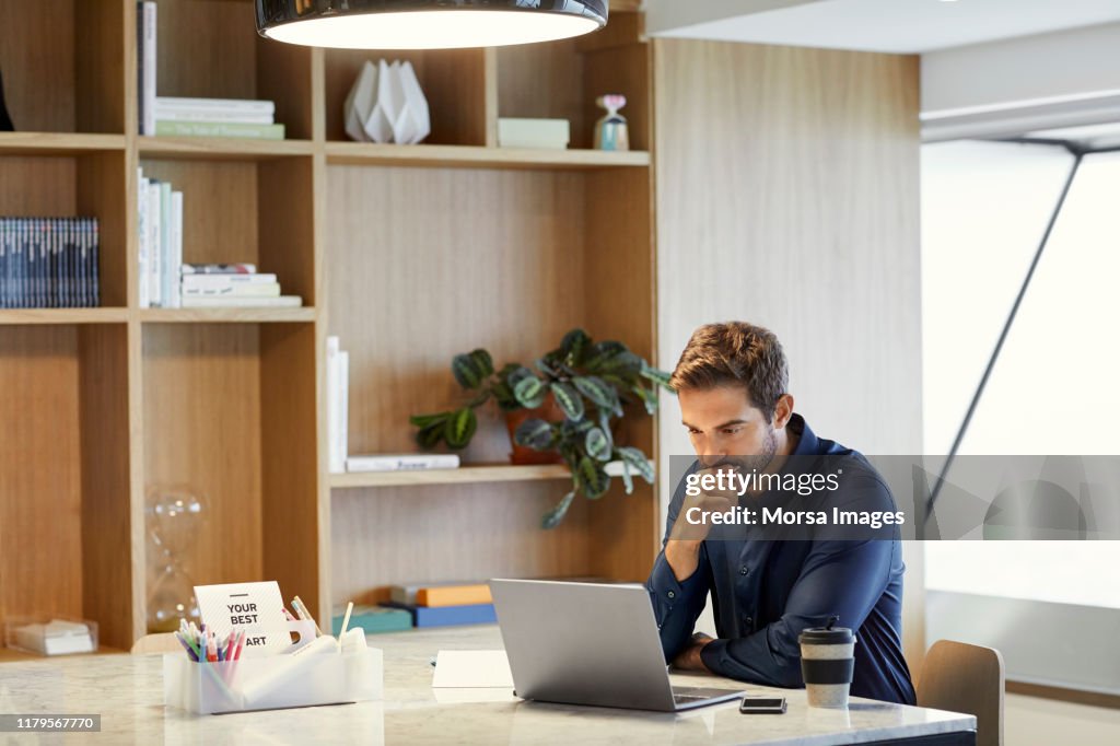 Serious businessman using laptop at office desk