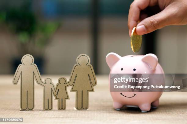 hand putting money coin into piggy bank and family paper on table - family budget stock-fotos und bilder