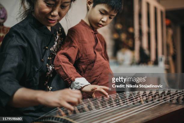 chinese grandmother and grandson in traditional clothes playing harp - zither stock pictures, royalty-free photos & images