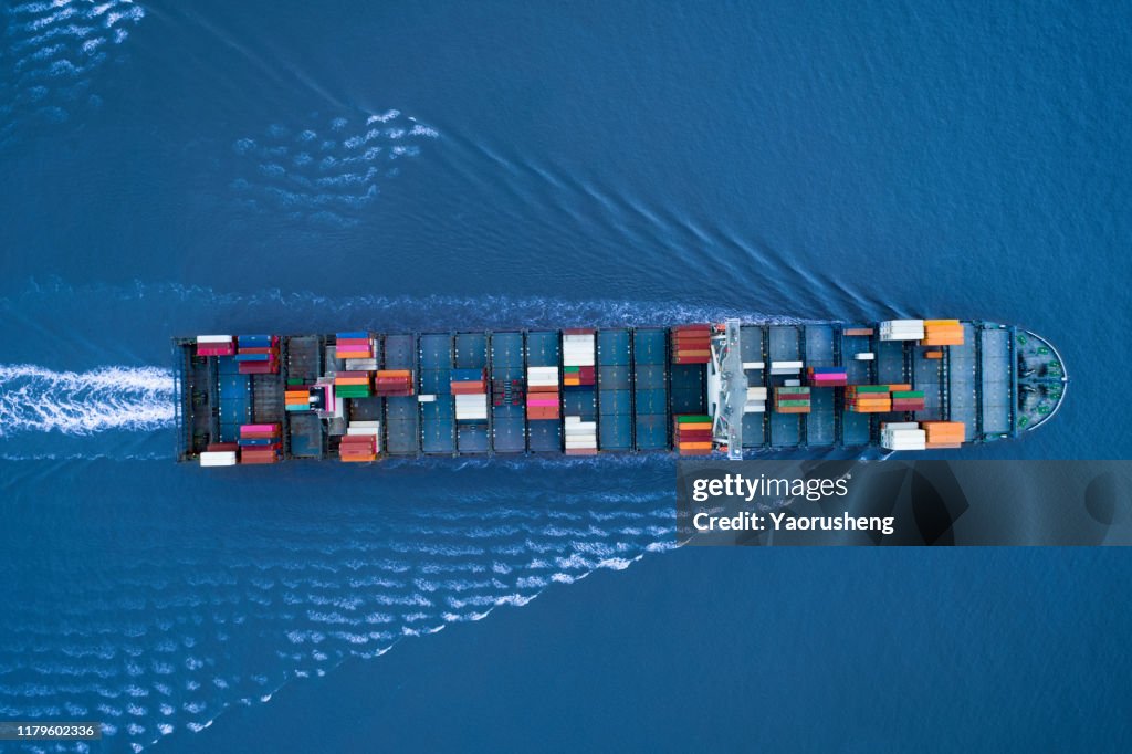 A Large container ship is approching the port full loaded with containers and cargo - aerial - top down view