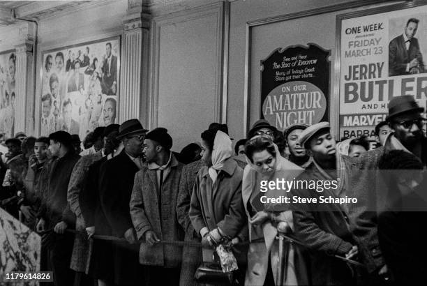 View of people lined up outside the Apollo Theater , New York, New York, 1961. Posters advertises a performance by Jerry Butler as well as Amateur...