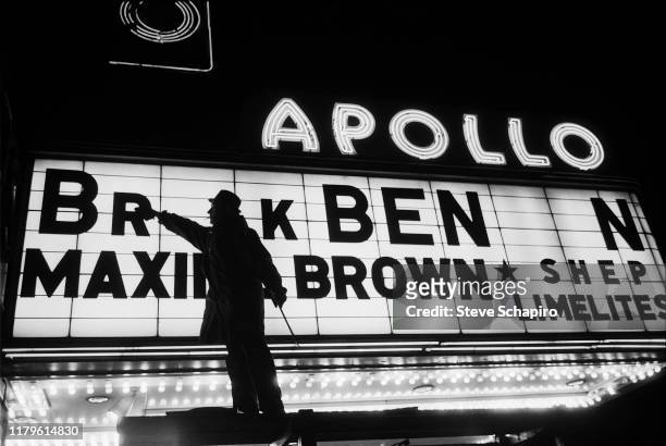 Nighttime view of a man as he changes the letters on the Apollo Theater marquee, New York, New York, 1961. The new sign, though incomplete, will...
