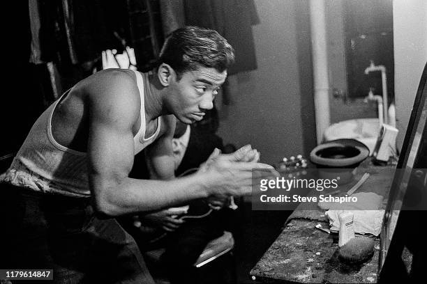 An unidentified man leans forward as he applies pomade in a mirror backstage at the Apollo Theater, New York, New York, 1961.