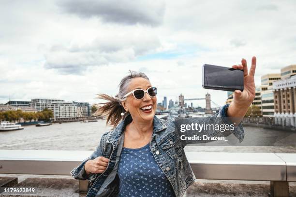 senior tourist in london macht selfie mit tower bridge im hintergrund - london und umgebung stock-fotos und bilder