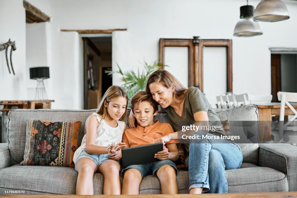 Mother showing digital tablet to children at home