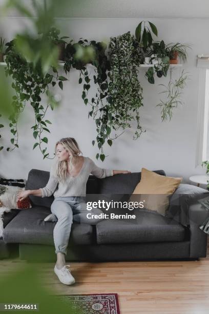young woman sitting in living room - plante tropicale photos et images de collection