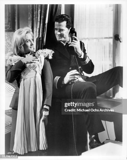 James Garner holding a telephone receiver while smiling at Liz Fraser holding a dress in a scene from the film 'The Americanization of Emily', 1964.