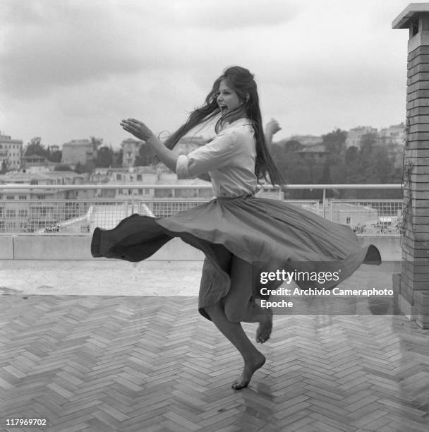 Italian actress Claudia Cardinale, wearing a shirt and a wide skirt, dancing barefoot on a roof terrace in Rome, 1959.