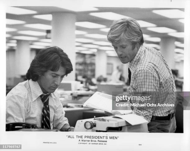 Robert Redford holding papers while speaking to Dustin Hoffman typing on a typewriter in a scene from the film 'All the President's Men', 1976.