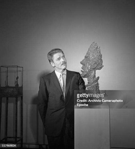 American actor Burt Lancaster, wearing a pinstriped suit and a tie, portrayed while standing next to Alberto Giacometti's sculpture 'La Grande Tete...