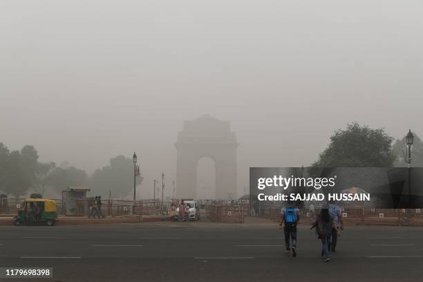 Tourists cross a road to visit the India Gate under heavy smog conditions, in New Delhi on November 3, 2019. - India's capital New Delhi was...