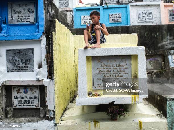 Young boy sits on top of a tombstone in a cemetery. Filipinos flock to cemeteries around the country to visit departed relatives and loved ones to...