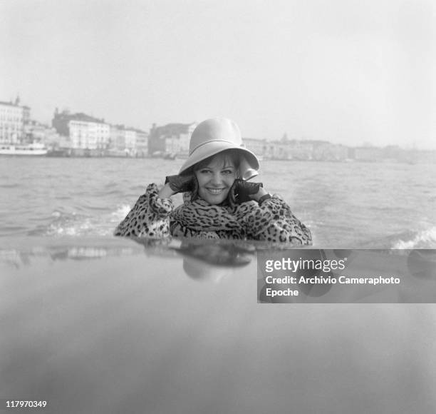 Italian actress Claudia Cardinale, wearing a fun fur and a hat, portrayed on a taxi boat, leaning on the roof top, St Mark's basin, Venezia 1958.