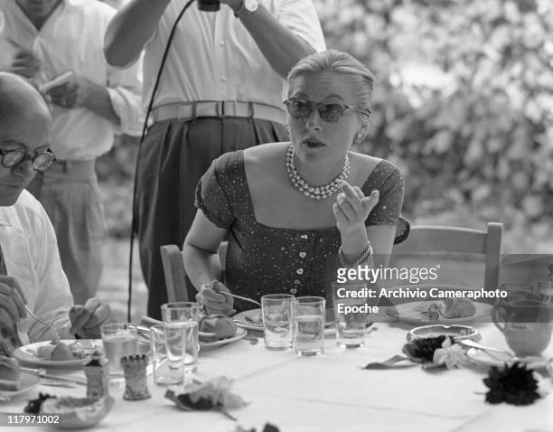 American actress Joan Fontaine wearing a fancy dress, a pearl necklace and sunglasses, sitting at a restaurant table outdoor in Torcello island,...