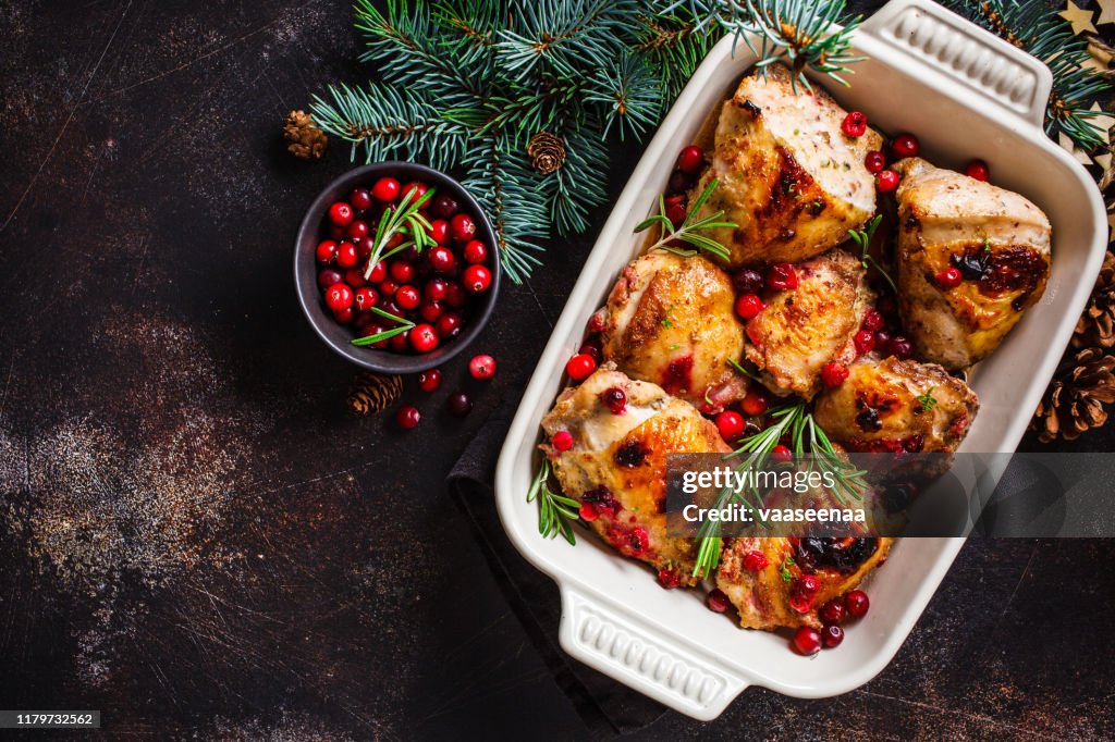Christmas food. Baked Chicken meat with cranberries and rosemary in the oven dish, dark background, copy space.