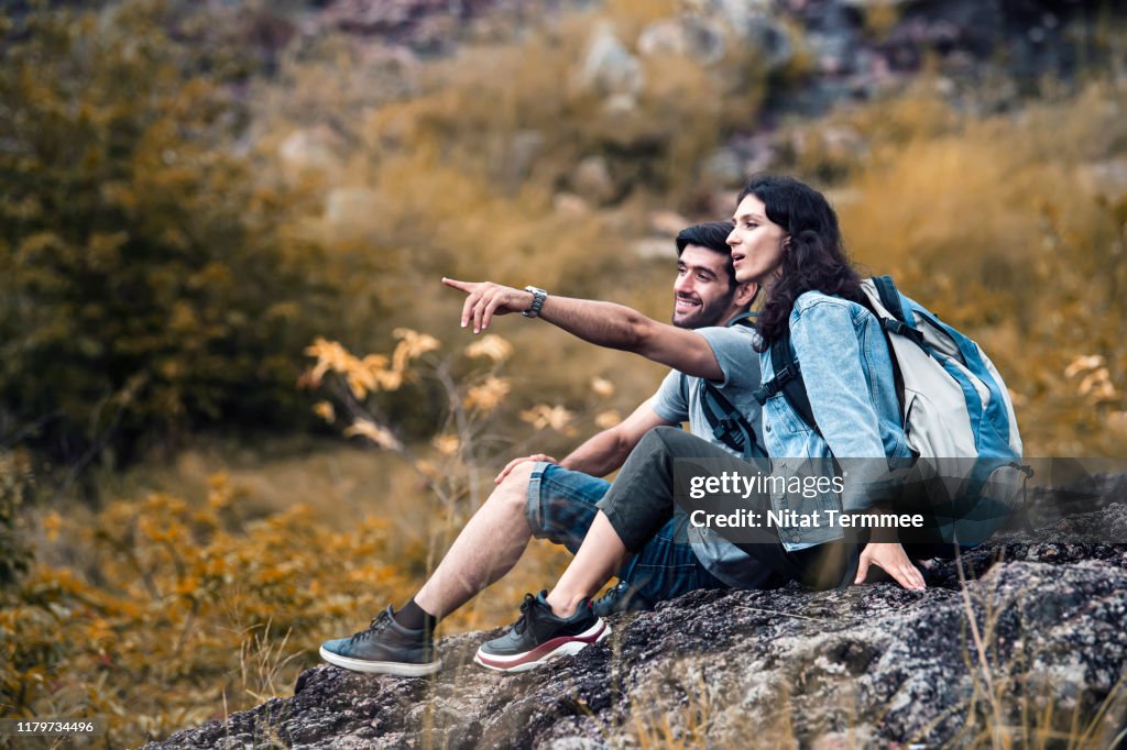 Happy young couple sitting on rock cliff outdoors on nature. Young couple travel on vacation during fall.