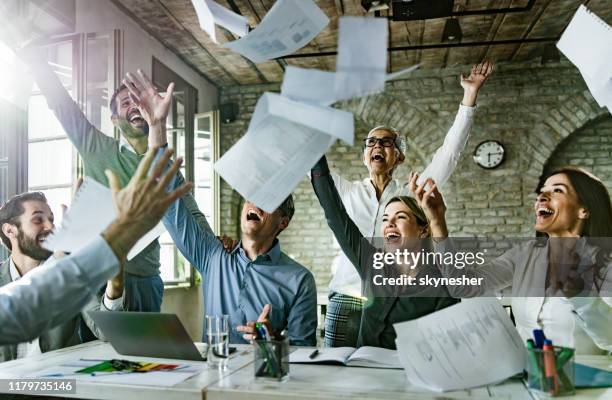 group of playful entrepreneurs having fun while throwing paperwork in the office. - good news stock pictures, royalty-free photos & images