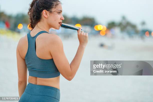 ung kvinna tar en paus från jogging, äta protein bar - open workouts bildbanksfoton och bilder