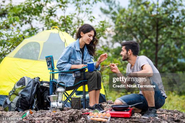 young couple enjoy cooking breakfast at camping stove on rock cliff outdoors on nature. - campingstuhl stock-fotos und bilder