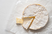 Camembert with two wedges cut out isolated on white wax paper wrapping. Top view. Space for text.