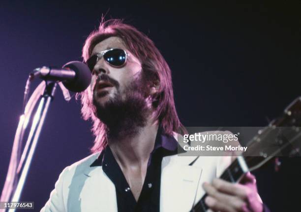 Eric Clapton, British guitarist, singing into a microphone and playing an acoustic guitar on stage during a live concert performance at the Nassau...