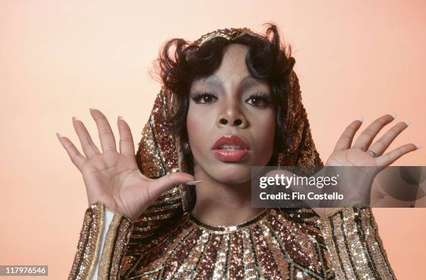 Headshot of Donna Summer, US singer-songwriter, posing in a studio portrait, with her hands raised, open-palmed, either side of her head, wearing...