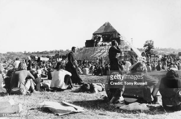 Two priests walking amonmg the crowds of festival-goers pictured from behind looking toward the Pyramid stage at the Glastonbury Festival, at Worthy...