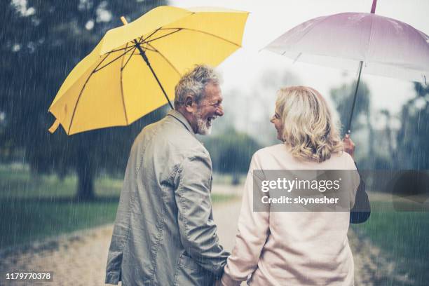 vue arrière du couple aîné heureux avec des parapluies prenant une promenade le jour pluvieux. - se protéger de la pluie photos et images de collection