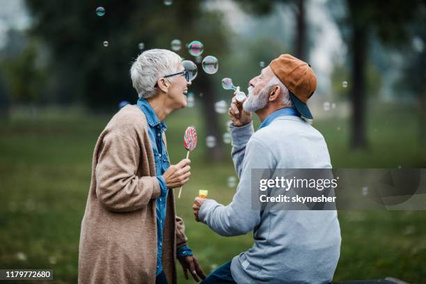 giocosa coppia senior che soffia bolle dalla bacchetta a bolle al parco. - blowing bubbles foto e immagini stock