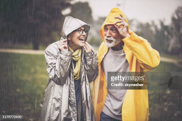 gelukkig volwassen paar in regenjassen tijdens regen in het park. - weather stockfoto's en -beelden