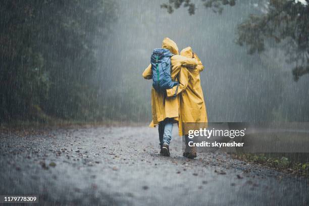 achteraanzicht van omarmd paar in regenjassen wandelen op een regen. - rainy day stockfoto's en -beelden