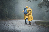 Back view of embraced couple in raincoats hiking on a rain.