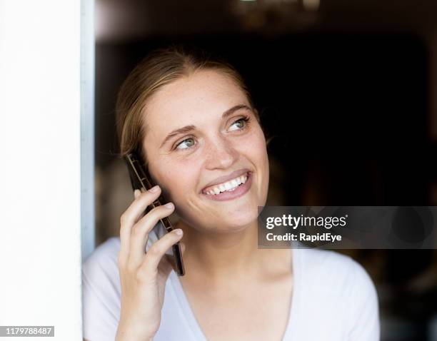 smiling, beautiful young woman using her mobile phone in the doorway of a store - woman ear to door stock pictures, royalty-free photos & images
