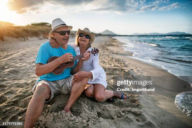 senior genießt musik am strand - ukulele stock-fotos und bilder