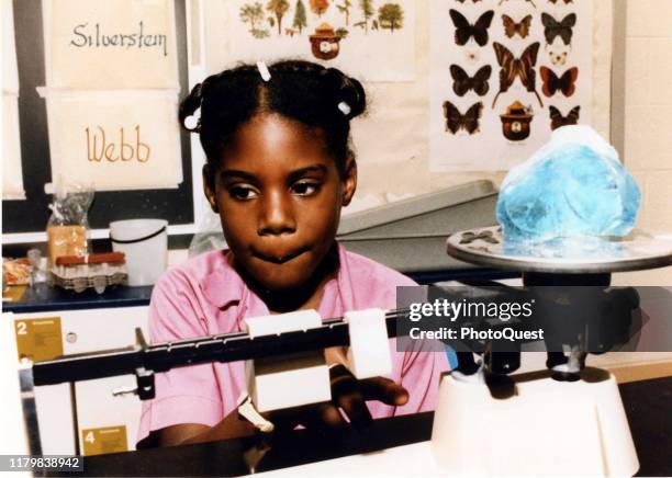 View of a young girl as she weighs a mineral sample in her elementary school classroom as part of special course work designed to involve students in...