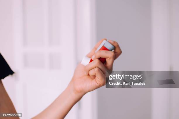a young woman is using an asthma inhaler device at home - inalador preventivo para asma imagens e fotografias de stock