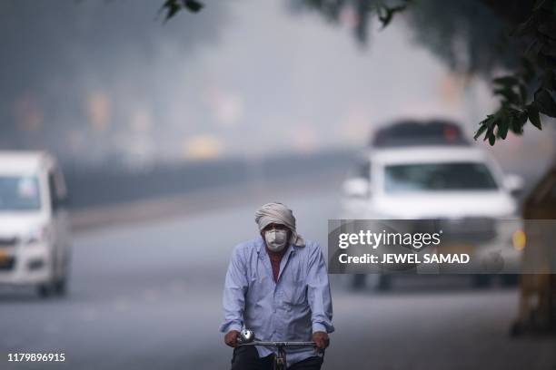 Man wearing protective face mask rides a bicycle along a street in smoggy conditions in New Delhi on November 4, 2019. Millions of people in India's...