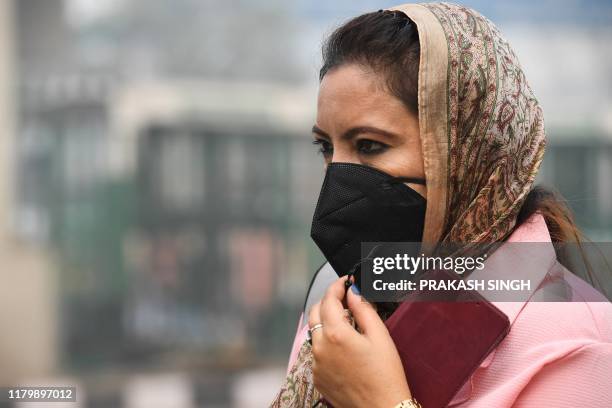 Woman wearing a protective face mask waits for public bus in smoggy conditions in New Delhi on November 4, 2019. - Millions of people in India's...